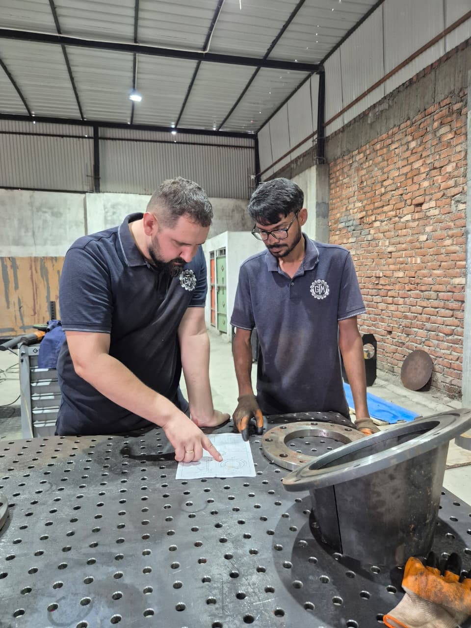 MD and technician reviewing engineering drawing on welding fixture table